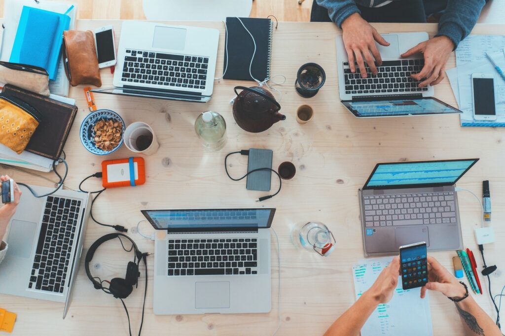 Multiple laptops, tablets, and phones sit on a table