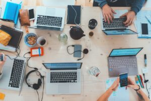 Multiple laptops, tablets, and phones sit on a table